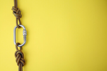 One metal carabiner with ropes on yellow background, top view. Space for text