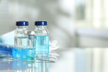 Glass vials, syringe and medical masks on white table, closeup. Space for text