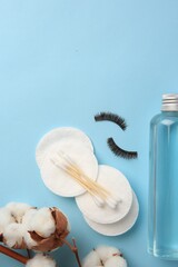 Fototapeta na wymiar Bottle of makeup remover, cotton flowers, pads, swabs and false eyelashes on light blue background, flat lay. Space for text