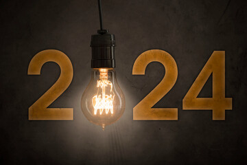 Close up of a bright light bulb with number 2024 on concrete wall background - obrazy, fototapety, plakaty