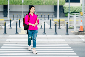 Full length front shot of an Asian female student in jeans with a backpack crossing the road