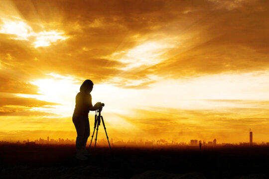 Female photographer taking landscape photo of city during sunset or sunrise