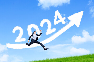 Business woman jumping over arrow sign with 2024 on the grass