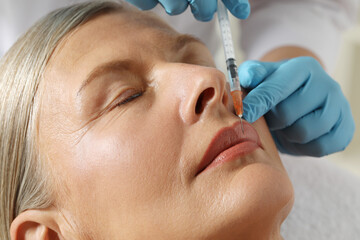 Doctor giving lips injection to senior woman in clinic, closeup. Cosmetic surgery