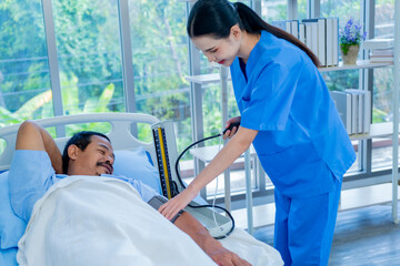 Obraz premium Asian nurse with tonometer measuring senior man patient's blood pressure at hospital