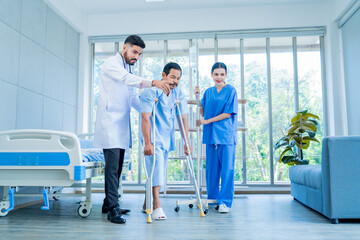 A Muslim male doctor and nurse help a patient who is doing physical therapy and is practicing walking with a walking stick.
