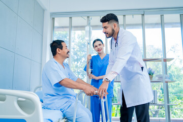 A Muslim male doctor and nurse help a patient who is doing physical therapy and is practicing walking with a walking stick.