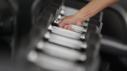 Slow motion close up of woman picking up free weight from dumbbell rack at fitness center - Powered by Adobe