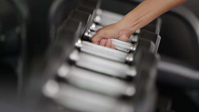 Slow motion close up of woman picking up free weight from dumbbell rack at fitness center