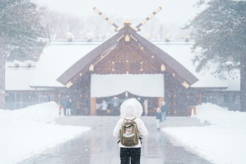 Woman tourist Visiting in Sapporo, Traveler in Sweater looking Hokkaido Shrine with Snow in winter...