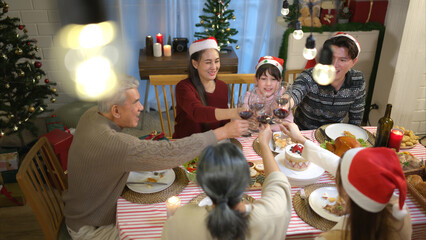 Happy asian family celebrating Christmas together at home. Cheerful senior parents and children in Santa hat clinking glasses of red wine.