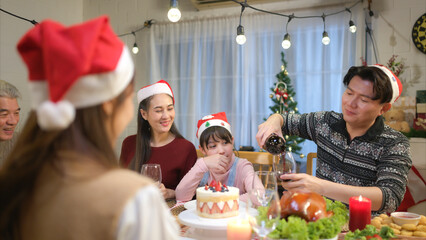 Happy asian family celebrating Christmas together at home. Cheerful senior parents and children in Santa hat clinking glasses of red wine.