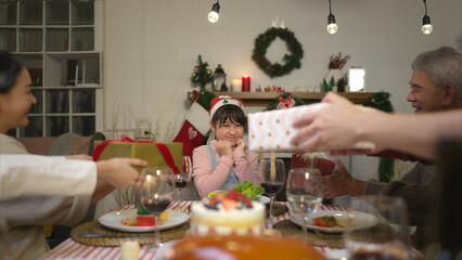 Little girl receives gifts from her family members during Christmas dinner at home.