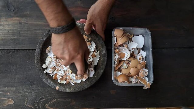 A man's hand is crushing an egg shell using a mortar. Pounded eggshells can be used as fertilizer.	