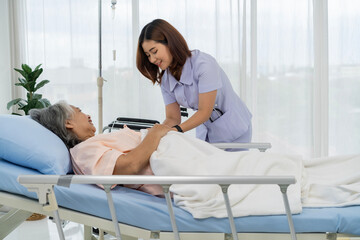 A nurse or caregiver of an elderly patient is helping to cover blanket a patient lying in bed. - 669793570