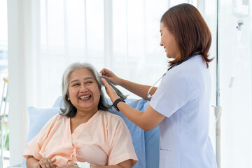 A nurse combs the hair of an elderly Asian patient and offers a pep talk.