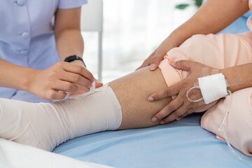 Fototapeta premium Close-up photo of an Elderly Asian patient admitted to hospital A nurse cares for a patient's injured leg bandage.