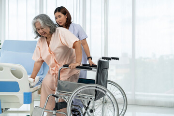A nurse carries an elderly Asian patient into a wheelchair to take him to get an x-ray of his leg injured in an accident.