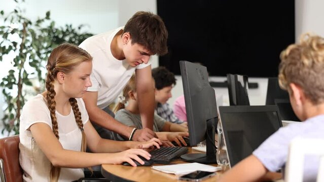 Concerned preteen girl sitting at computer while trainer explaining him something during IT courses 