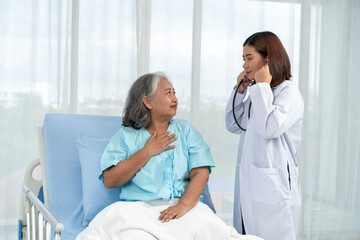 Female doctor uses stethoscope to check lung breathing for elderly Asian female patient. - obrazy, fototapety, plakaty