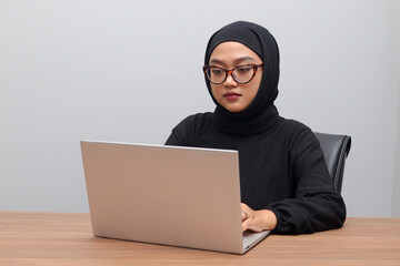 Portrait of attractive Asian hijab woman working on her laptop. Muslim girl doing task in office....