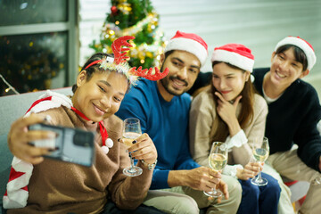 Obraz premium Group of diverse ethnicity young people enjoy celebrating a Christmas and New Year party together with a lot of foods and drinks. Woman enjoy taking a selfie photo on mobile phone with a friends.