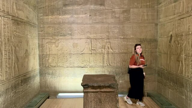 Tourist girl exploring and touching hieroglyphs inside temple of Horus in Edfu, Egypt. Egyptian Temple of god Horus in Edfu. Ancient Egypt monument. walls with herogliphs in egyptian religious temple