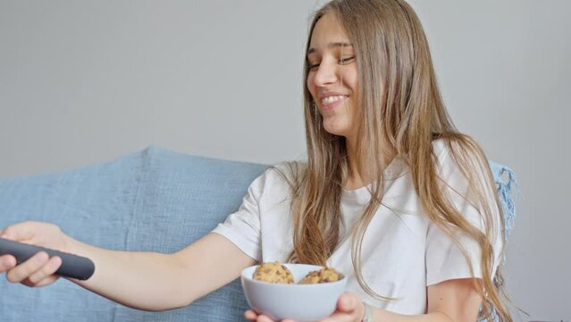 Girl watching comedy, holds chocolate biscuits and using tv remote, stable shot