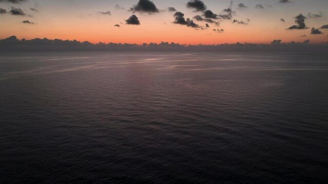 Drone flying backwards during beautiful orange sunrise over calm sea
