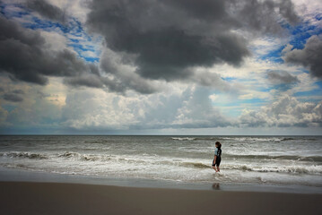 Young child standing in the ocean during cloudy storm