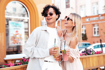 Young smiling beautiful woman and her handsome boyfriend in casual summer clothes. Happy cheerful family. Female having fun. Couple posing in street. Holding and drinking cocktail drink in plastic cup