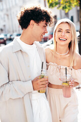 Young smiling beautiful woman and her handsome boyfriend in casual summer clothes. Happy cheerful family. Female having fun. Couple posing in street. Holding and drinking cocktail drink in plastic cup