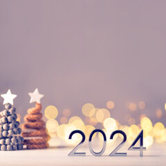 Metal numbers 2024 on a white table with Christmas trees and bokeh lights. Happy New Year 2024 is...
