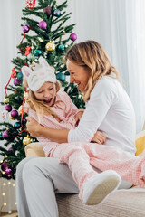 Mother hugging cute daughter in pajamas and laughing. Christmas holidays at home.
