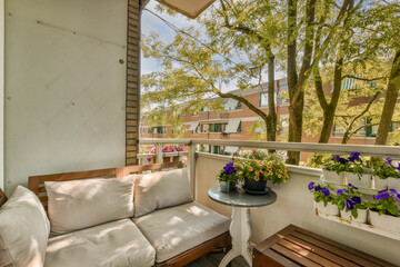 a balcony with flowers and plants on the outside furniture, as seen from an open window in this...