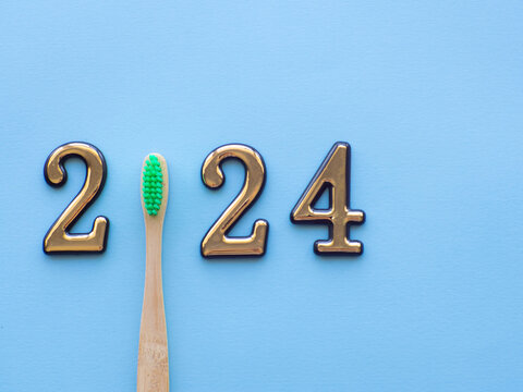 2024 and dental concept. Close up view photo with 2024 and wooden green toothbrush instead zero on blue background with copy space for text. Christmas medical card. Merry Christmas and Happy New Year