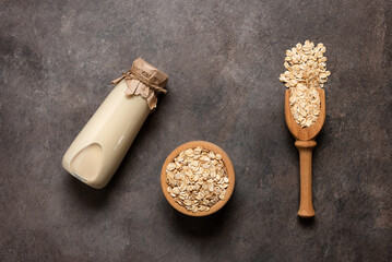 Oat milk in a bottle and oat flakes on a dark rustic background. Top view, flat lay, copy space.