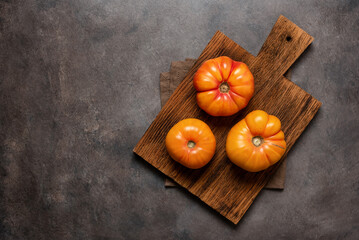Fresh yellow tomatoes on a wooden cutting board. Top view, flat lay. Dark rustic background.