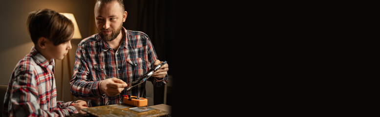 Father and son repairing motherboard at home in the evening, father teaches son how to use a...