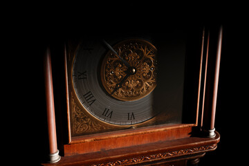 Close-up of the dial of an antique grandfather clock in a dark room, illuminated by light from the...
