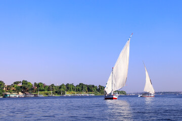 Obraz premium Traditional sailing boat felucca, Nile river near Aswan, Egypt. A famous tourist attraction - sailing boat ride