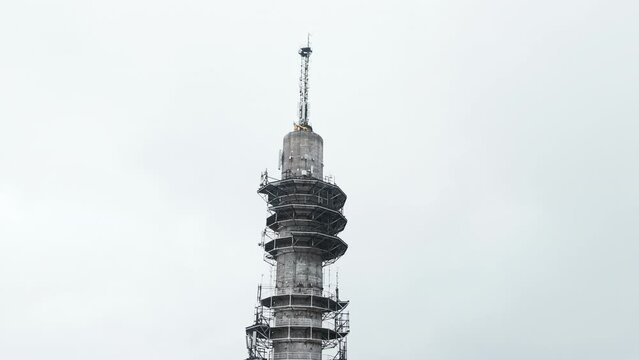 Aerial close up moving to a wide shot of a bleak industrial concrete television and radio link tower in Pasila, Helsinki, Finland on a bright and foggy day. Apartment buildings in background.