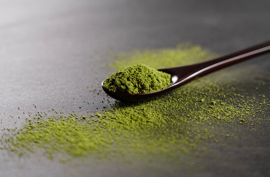 Matcha and wooden spoon on black background.