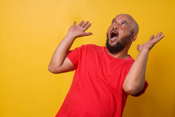 Bearded bald man feeling shocked and surprised while looking up with raised hands