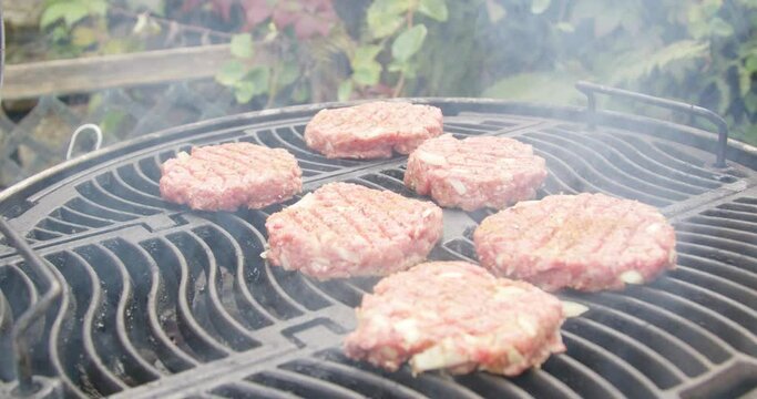 Closeup footage of putting the raw beef burgers on a portable charcoal grill with a spatula outdoor