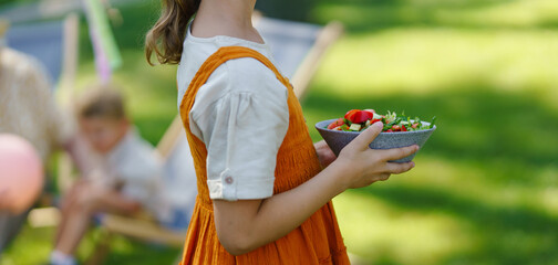 Close up of young girl setting table for summer garden party. Girl holding plate with fresh...