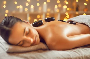 Cercles muraux Spa Portrait of young woman having spa hot stone massage in beauty salon. Relaxed pretty girl lying on couch with black basalt stones along spine. Beauty treatment therapy, body care concept