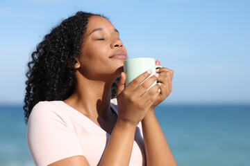 Black woman smelling coffee on the beach