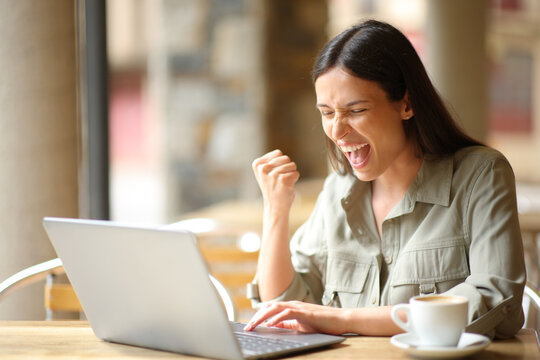Excited woman celebrating in a restaurant checking laptop