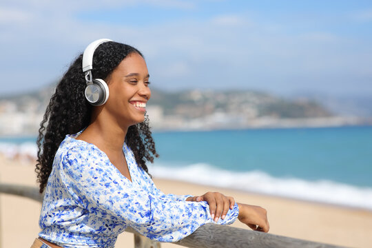 Happy black woman listening music on the beach